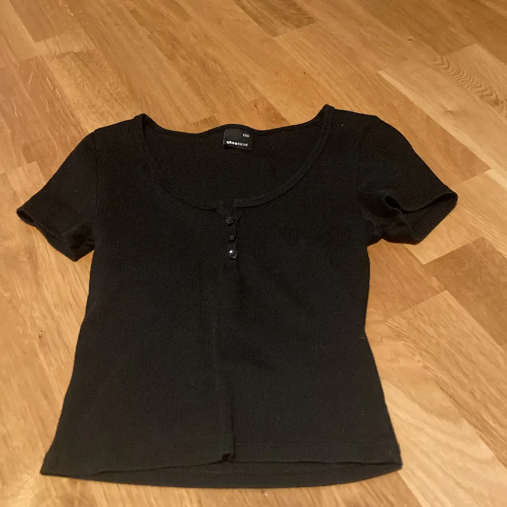 Svart t-shirt med knappar och randigt material . T-paidat.