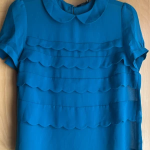 Skir blus med volanger  - Skir tunn festlig blus med krage och knapp på baksidan och ärmarna. Aldrig använd helt ny. Snygg diesel blå/grön tyg lätt genomskinlig 