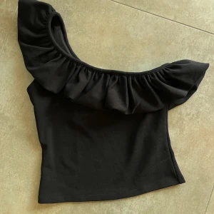 H&M svart off shouldef top strl S - Superfin, svart off shoulder topp med volang från H&M. Helt oanvänd med lappar kvar. 95% polyester, 5% elastan.