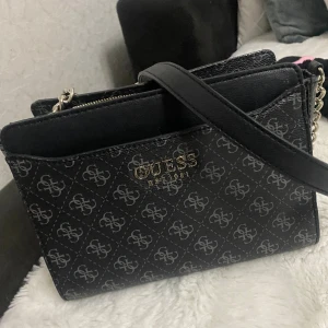 Guess väska  - Säljer denna fina väska av märket Guess. Den är som ny och använd någon enstaka gång bara och därav i jättefint skick. Jag köpte den för 1400 på och säljer den för 550. Den har ett band och det rymmer mycket i den:)