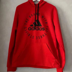 Hoodie från Adidas - En röd hoodie från Adidas med svart tryck på framsidan och armarna. Den är knappt använd och i mycket bra skick. Storleken är S och följer kroppen väldigt bra