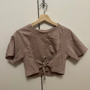 Gymshark helt ny croppad t-shirt - Aldrig använd croppad t-shirt från Gymshark! Två band man knyter åt u midjan och fina detaljer på hela tröjan! Gymshark loggan på ena sidan. 