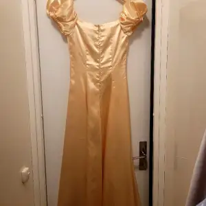 Detta är en balklänning som påminner Belle's dräkt i filmerna. Färgen är guldaktig/mjukt gul och materialen ger både struktur och glans. Den sitter åt i midjan och skapar visuellt en⌛ shape, men synd inte så bra pga att den inte sitter påklädd. 