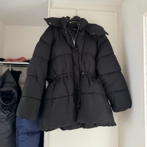 Jacka - Jacka ifrån Gina tricot.  Pufferjacka med huva. Jackan är svart och har något oversized passform. Den har dragkedje- och tryckknappsstängning fram, elasticerade dragskor i midjan och fickor i sidorna. Knappt använd och är slutsåld nypris 899 kr
