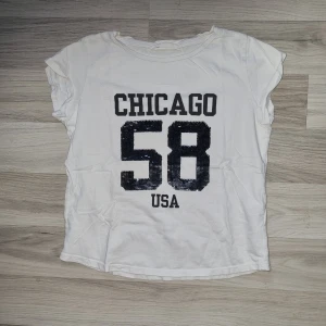 Vit t-shirt med tryck 'CHICAGO 58 USA' - En vit t-shirt med paljetter som man kan vända på 'CHICAGO 58 USA' på framsidan. T-shirten har korta ärmar och en rund halsringning. Från H&M i stl 146/152