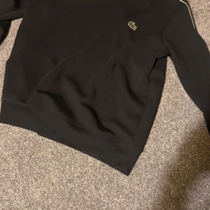 Lacoste Sweatshirt Black/Limiera - Inte så mycket använd, den är i storlek M men passar även L då den sitter lite lösare vid midjan. Köpt från zalando 