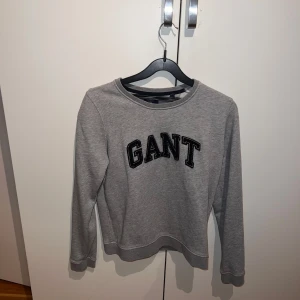 Grå tröja från GANT - En grå tröja från GANT med svart text på framsidan. Tröjan har långa ärmar och en rund halsringning.