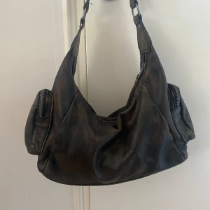 Väska - Liten och cool väska med brunrostig färg! Köpt på Asos för ett år sen och är knappt använd🌟 väldigt bra skick. Den har dragkedja och två små fack på sidorna med dragkedja. Höjd 17 cm, bredd: 27 cm, djup: 7,5 cm