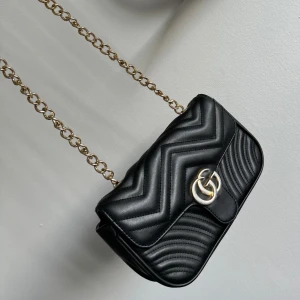 Axelremsväska svart med guld och silver - Äkta läder, aldrig använd. Superfint skick, säljs pga kommer aldrig till användning. Lagom mycket utrymme, långt band.  