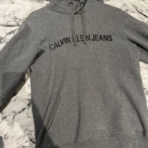 Calvin Klein hoddie - Säljer en jättefin, grå, varm hoddie från Calvin Klein Jeans i stl. S. (Någon skråma på bild 3, men ej märkbar därav priset) Använd fåtal gånger och säljer för 120kr+frakt. (Kan i vissa fall mötas upp)😊
