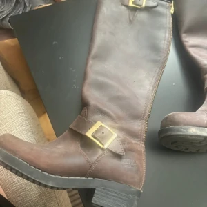 Bruna skinnstövlar från Johnny Bulls - Ett par bruna läderstövlar från Johnny Bulls med dragkedja och spänne. Stövlarna har en robust design med en låg klack och är tillverkade i högkvalitativt läder