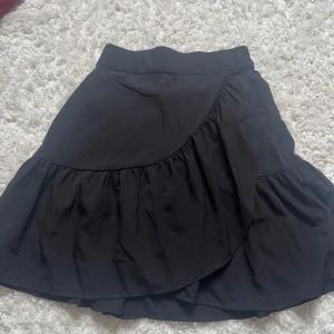 Lindex Kjol - Säljer denna söta svarta omlott kjolen från Lindex. Knappt använd så i super gint skick. Skriv privat om du har frågor eller funderingar.