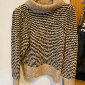 Randig stickad tröja - Beige och svartrandig stickad tröja från det danska designermärket, Copenhagen Muse. Bred polokrage och lite puffiga ärmar. Storlek S men kan även passa och liknar M. Pris kan självklart diskuteras!