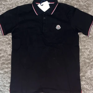 Moncler piké  - Säljer denna fina moncler piké som är i svart färg och i storlek Large. Tröjan har aldrig  använts och är i nytt skick.