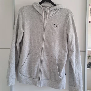 Grå hoodie från Puma - En bekväm grå hoodie från Puma med dragkedja framtill. Hoodien har en justerbar huva med dragsko och två framfickor. Den är långärmad och har ribbstickade muddar vid ärmslut och nederkant. Passar s/m🤍🤍