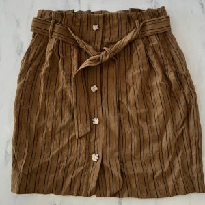 Brun kjol från H&M - En brun kort kjol med svarta ränder med avtagbart band/bälte. Har även fickor! Stängs med hjälp av en dragkedja på sidan, ej stretchig. Från H&M i storlek 42. Har bara hängt i min garderob så den är endast testad ❣️