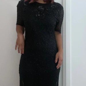 Vintage Svart Paljett Klänning   - Storlek: Large  Längd: jag är 1,5 lång och klänningen går nedanför min knäskål  Svart vintage klänning emblerad med pärlor och paljetter. Blommor broderade fram och bak med fina detaljer vid kjolens slut.  