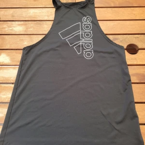 Svart linne från Adidas - Ett svart linne från Adidas med deras logotyp tryckt i vitt på framsidan. Linnet är ärmlöst och tillverkat i ett lätt och andningsbart material, perfekt för träning. Aldrig använt.