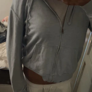 Grå hoodie med dragkedja - En bekväm grå hoodie med dragkedja framtill. Jackan har långa ärmar och en avslappnad passform, perfekt för vardagsbruk.