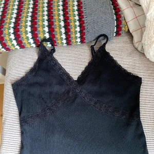 Kort svart topp med spets!  - Kort svart topp med spets från bikbok. Bra skick då jag knappt har använt den. Kort och har spets! Skönt material och passar till allt. Den har justeringsspännen så man kan ändra längden på banden! 