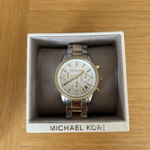 Michael Kors klocka  - Säljer en Michael Kors klocka i modellen RITZ i silver/guld. Den är i fint skick och har inga repor på uret. Extra länkar och kartong medföljer. Nypris är 2695 kr.