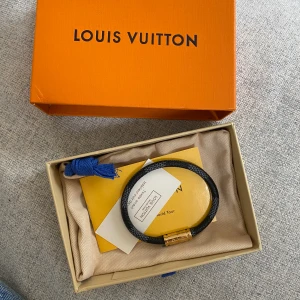 Louis vuitton armband  - Louis vuitton armband svart grå färg med en magnet som binder ihop armbandet 