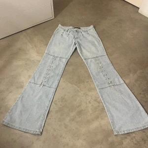 Lågmidjade utsvängda jeans med snöre  - Super fina ljusblåa byxor med coola detaljer på knäna. Står storlek 25 men skulle säga att dem passar på S-M