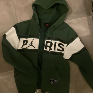 Jordan x Paris Saint-Germain Zip-Up Hoodie - Säljer en snygg och unik Jordan x Paris Saint-Germain (PSG) zip-up hoodie i grönt. Denna hoodie är perfekt för både vardagsbruk och att visa upp din kärlek för sporten och mode.