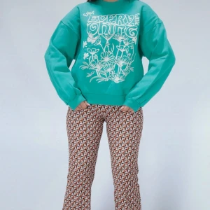 Grön sweatshirt med blommönster,L - En bekväm grön sweatshirt med ett vitt blommönster och texten 'Enjoy Every Little Thing' på framsidan. Tröjan har långa ärmar och ribbstickade muddar vid ärmslut och nederkant.i mycket fint skick, oversized tröja och passar S/M också 