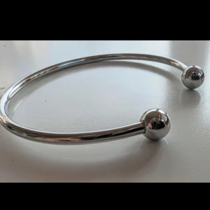 Silverfärgat armband med kulor - Ett stilrent armband i silverfärg med två kulor i ändarna. Armbandet är öppet och kan justeras för att passa olika handledsstorlekar. Perfekt för både vardag och fest.i rostfritt stål 