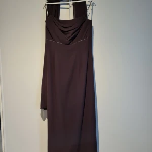 Balklänning i plommon - Den är andvänd en gång för ett bröllop och har sedan dess hängt mörkt i sin förvaringspåse. Den har väldigt vacker klassisk design och är av märket blue crown fashion och kostade 2800kr ny Väska ingår. Armhåla till armhåla 46cm Midja 92cm Längd 132cm