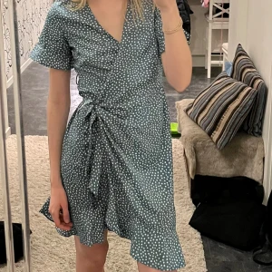 Omlottklänning turkos - Turkos/blå omlottklänning med prickigt mönster från Vero moda. Säljer då jag endast använt den 2 gånger! 