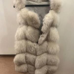 Vit/grå pälsväst stl. M - En äkta pälsväst vit/grå färg i storlek M. Den är knappt använd och i gott skick förutom några få små fläckar inuti men inget på utsidan. Säljer den för 1700kr.  Kan mötas upp i Stockholm men även skicka västen, dock står du för frakt.  