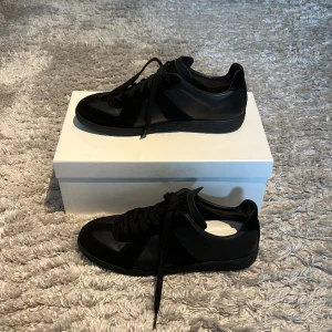 Maison Margiela GAT - Maison Margiela GAT i stl 42. Black on black i fint skick. Använda ca 10 ggr. Box + travel skydd ingår. Nypris €520 (ca 5800kr). Köpta från Mytheresa. Just denna colourwayen är slutsåld på mytheresa och hittar endast den på Cettire för 5200kr. 
