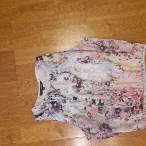 Blommig blus från KappAhl - Söt blommig blus från KappAhl i ljusa pastellfärger med inslag av rosa, beige och vitt. Ärmlös modell med knytning framtill och mjukt, luftigt tyg som passar perfekt för varma dagar. Romantisk och feminin stil med vackert blommönster.