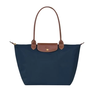 Marinblå väska från Longchamp - Snygg marinblå axelväska från Longchamp med klassisk design. Väskan har bruna skinnhandtag. Tillverkad i slitstark polyester och skinn, perfekt för att bära allt du behöver i vardagen.