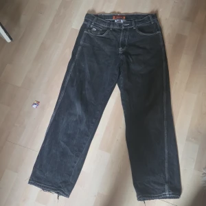 Svarta wide jeans från Butter, strl 30 - Svarta jeans från Butter med relaxed fit och breda ben. Snygga kontrastsömmar, tärningsdetalj på myntfickan och broderad figur på bakfickan. Jeansen har råa, fransiga benslut och klassisk femficksdesign. Perfekta för en chill och avslappnad stil.