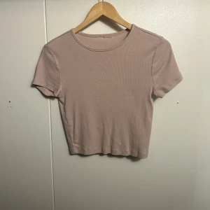 Beige ribbad croppad topp - Säljer en beige croppad topp med korta ärmar och rund hals. Toppen är ribbad och har en enkel, stilren design som är lätt att matcha. Perfekt för dig som gillar en clean och chill look.