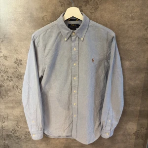 Ljusblå skjorta Polo Ralph Lauren slim fit - Säljer en klassisk ljusblå skjorta från Polo Ralph Lauren i slim fit. Skjortan har button down-krage, broderad logga på bröstet och knäppning framtill. Tillverkad i mjuk bomull och har långa ärmar. Perfekt för en clean och stilren look.