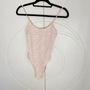 Ljusrosa spets body - Söt ljusrosa spets body med smala axelband och spetsdetaljer över hela plagget. Toppen är ärmlös och har en feminin, figurnära passform.