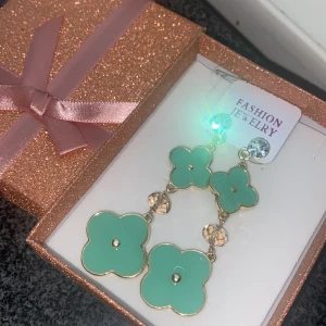 Mintgröna blommiga örhängen - Superfina hängande örhängen med mintgröna blommor och guldfärgade detaljer. Örhängena har glittrande stenar upptill och små pärlliknande dekorationer mellan blommorna. Perfekt att ge bort i den glittriga presentasken som ingår!