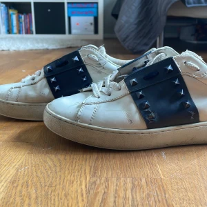 Valentino Rockstud sneakers vit/blå - Snygga Valentino Rockstud sneakers i vitt skinn med marinblå detaljer och ikoniska nitar. Skorna har snörning, platt sula och coola pyramidformade nitar både på sidorna och baktill. Perfekta för dig som vill sticka ut med en lyxig streetstyle. Pris kan diskuteras skriv om de är något om ni vill ha fler bilder så fins jag här👌🏻✅