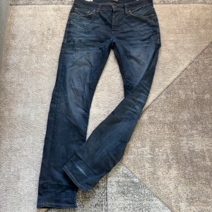 Jack & Jones Slim Straight Tim Jeans - Mörkblå jeans från Jack & Jones, modell Slim Straight Tim. Klassisk femficksdesign med snygga kontrastsömmar och läderpatch bak. Jeansen har rak passform med en något smalare siluett och är tillverkade i slitstarkt denimtyg. Storlek 30/32