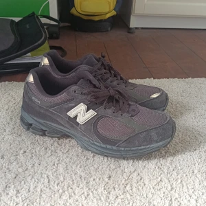 Mörkgrå New Balance 2002R sneakers - Säljer ett par mörkgrå New Balance 2002R sneakers med klassisk mesh och mocka på ovandelen. Skorna har tydlig N-logga på sidan, snörning och en chunky sula som ger skön dämpning. Perfekta för dig som gillar retrovibbar och streetstyle. Det vinröda aktikt är grått, det ör bara min kamera som är dålig‼️