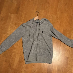 Grå hoodie från Polo Ralph Lauren - Klassisk grå Polo Ralph Lauren kofta med huva och dragkedja. Köpte den för ett par månader sedan och insåg att den var för liten för mig. Står att den är storlek M men känns mer som en S.