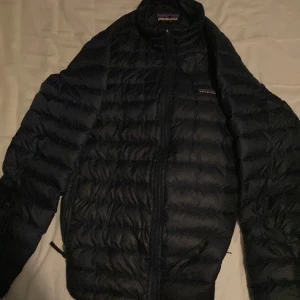 Svart dunjacka från Patagonia - Säljer en svart dunjacka från Patagonia med quiltad design och dragkedja framtill. Jackan är lätt och smidig, perfekt för kyliga dagar. Tillverkad i polyester med fyllning av ankdun och fjädrar. Klassisk logga på bröstet och hög krage. ‼️⁉️Är öppen för byten ‼️⁉️