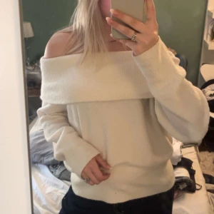 Offshoulder vit stickad tröja - Superfin offshoulder stickad tröja i vitt med bred krage som sitter snyggt över axlarna. Tröjan har långa ärmar och en loose fit, perfekt för att skapa en chill och trendig look. Mjuk och skön, passar perfekt till jeans eller kjol.