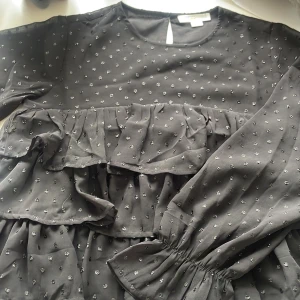 Svart volangblus, Gina Tricot - Supersöt svart glittrigvolagblus från Gina Tricot med glittriga prickar och flera lager volanger. Blusen har långärmade ärmar med lätt puff och rund halsringning. Andvänd fåtal gånger och är i bra skick. !pris kan diskuteras!
