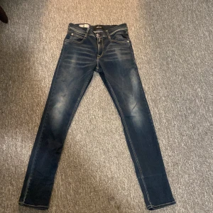 Replay Wallys mörkblå jeans - Säljer ett par mörkblå Replay Wallys jeans med snygga slitningar och kontrastsömmar. Modellen har klassisk femficksdesign, raka ben och coola detaljer på bakfickorna. Jeansen är tillverkade i stretchigt denim för extra komfort.