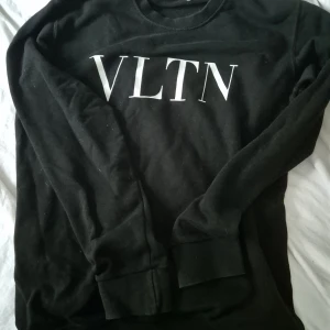Svart Valentino sweatshirt VLTN - Svart sweatshirt från Valentino med VLTN-tryck i vitt över bröstet. Klassisk rund halsringning och långa ärmar. Tröjan har en clean och stilren look, perfekt för dig som gillar designerplagg med enkel vibe.